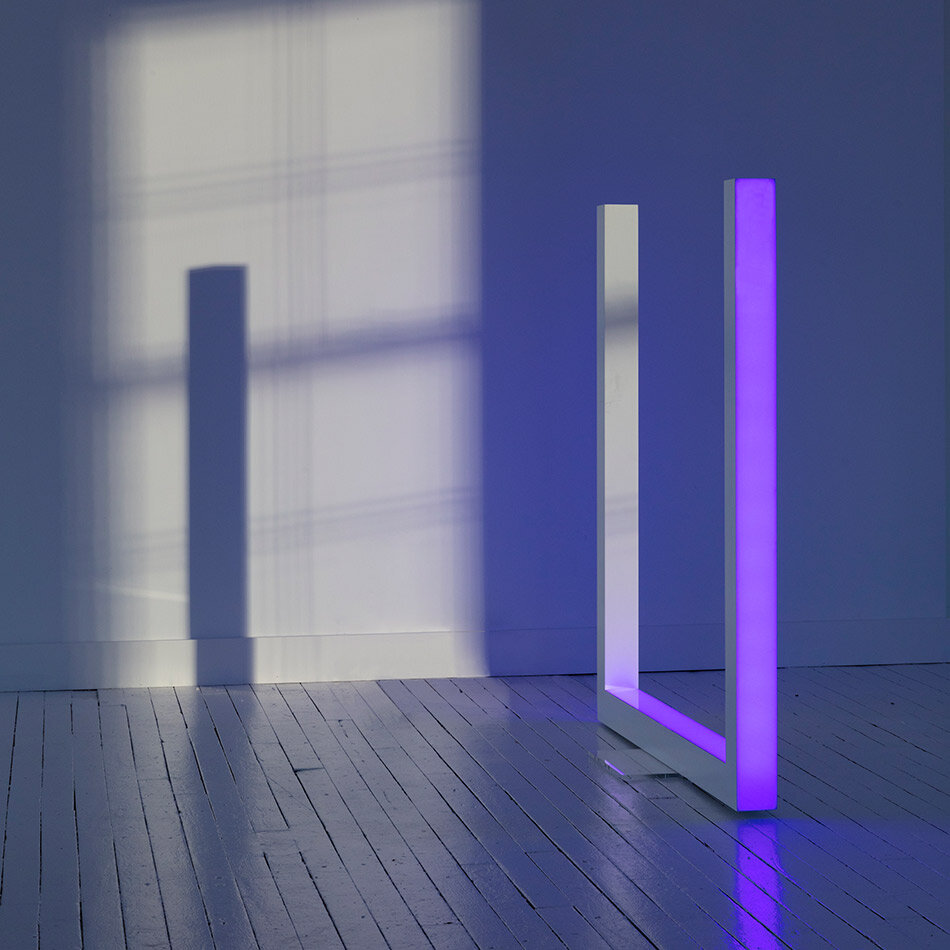 The U-shaped light sculpture illuminated violet beside the gallery window.