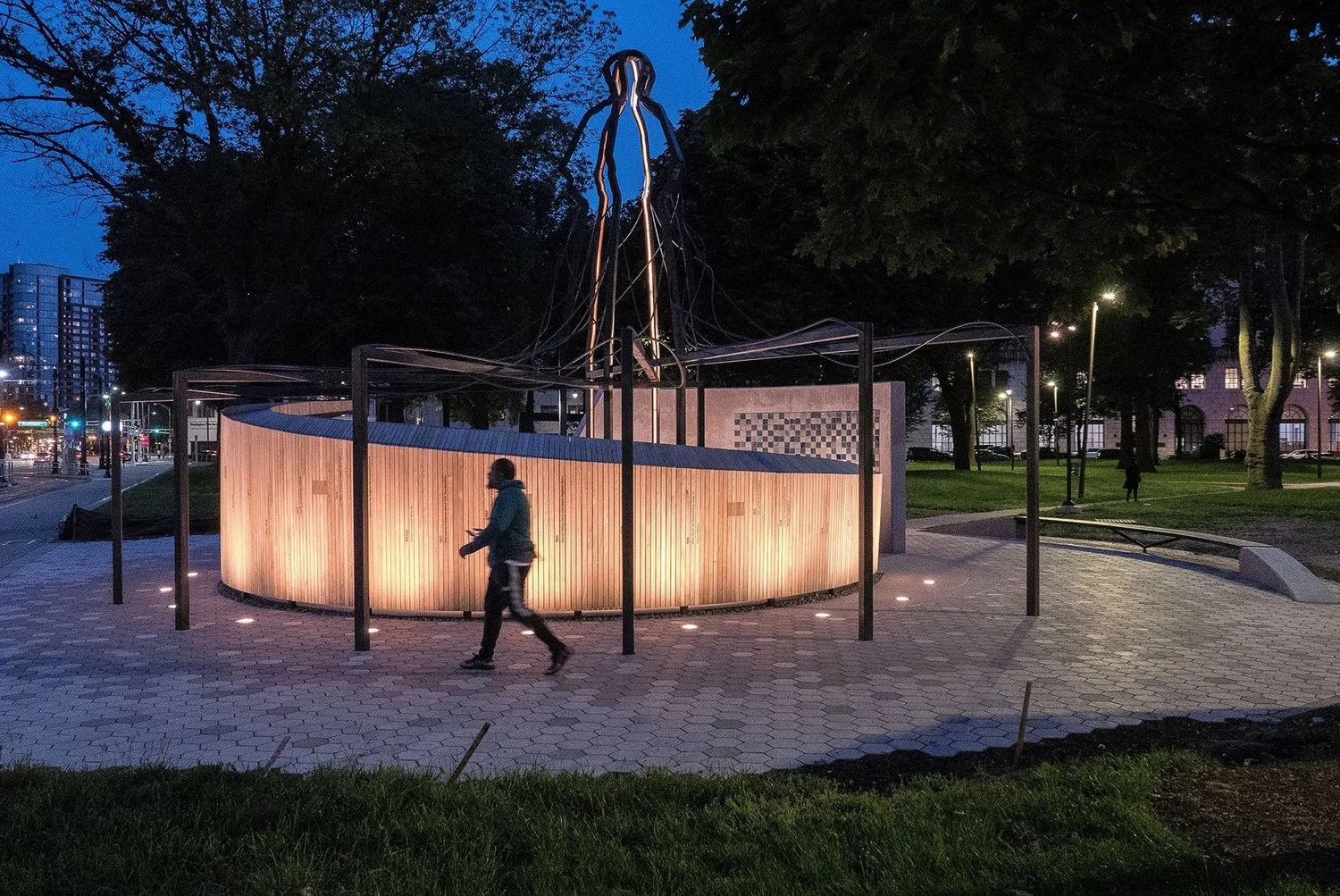 Shadow of a Face illuminated at blue hour in Newark, with a person walking past its curved wooden wall