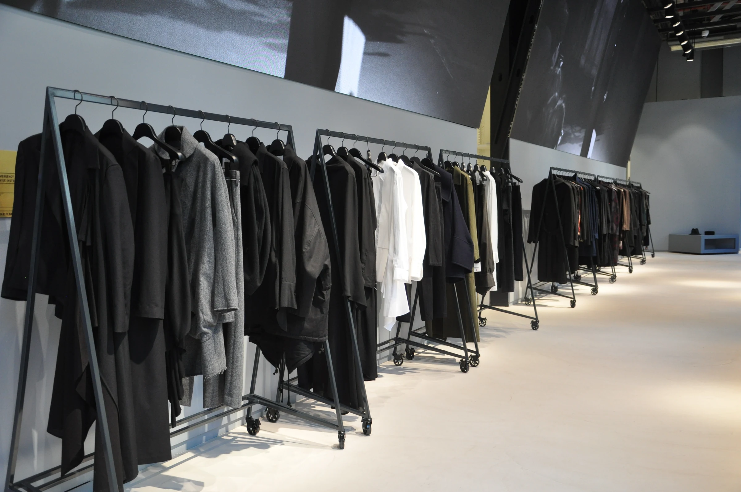 Steel clothing racks carrying garments along the wall of the finished Yohji Yamamoto store.